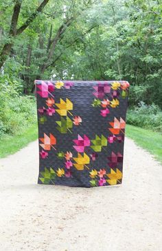 a black quilt with colorful leaves on it in the middle of a dirt road next to trees