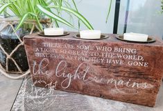 a wooden box with three candles on top of it and some plants in the background