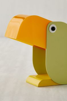 an orange, yellow and green bird lamp with eyes on it's head sitting on a white surface