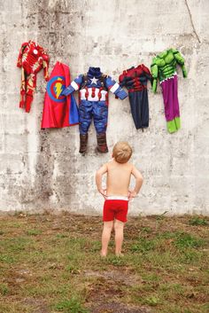 a young boy standing next to a wall with clothes hanging on it's side