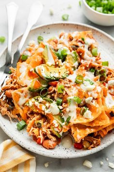 a white plate topped with nachos covered in cheese and toppings next to a bowl of green onions