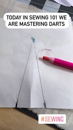 a pink pen sitting on top of a piece of paper next to a sewing needle