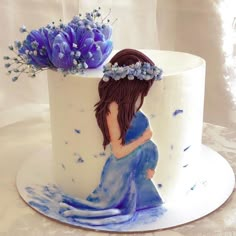 a white cake with blue flowers and a pregnant woman on the top is decorated in fondant