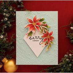 a christmas card with poinsettis and greenery on the table next to ornaments