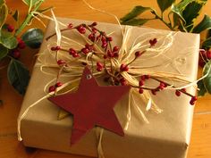 a present wrapped in white paper with a red star decoration on it and greenery