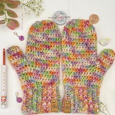 a pair of colorful knitted mittens sitting on top of a table next to a pen