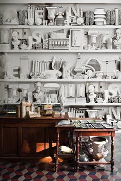 a room with shelves filled with lots of different items on top of each shelf and a wooden table in front of it