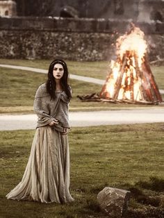 a woman standing in front of a fire with her hands on her hips and looking at the camera