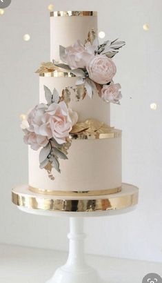 a three tiered wedding cake with pink flowers on the top and gold trimmings