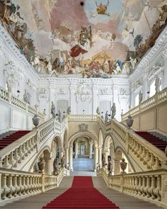 an ornate staircase with red carpet leading up to the upper floor and painted ceiling above it