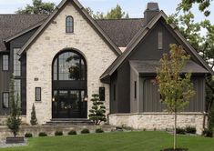 a large home with stone and black trim on the front door, windows, and landscaping