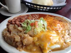 a white plate topped with lots of food next to a cup of coffee on a table