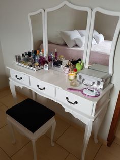 a white vanity with mirror, stool and makeup on the counter in front of it