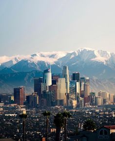 the city is surrounded by mountains and snow capped peaks in the distance, as well as palm trees