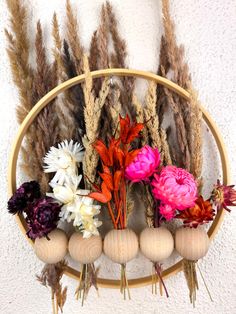 an arrangement of dried flowers and feathers in a circular wooden holder on a wall hanging