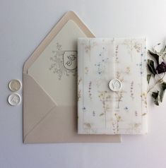 an envelope and some flowers on top of a white table with two silver coins next to it