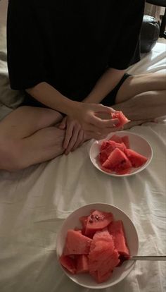 two white plates with slices of watermelon on them sitting on a bed next to each other