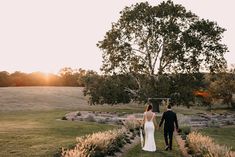 the bride and groom are walking down the path to their wedding ceremony at sunset in an open field