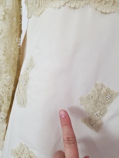 a woman's hand pointing at the back of a white dress with lace on it