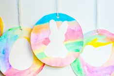 three painted easter eggs hanging from strings on a white wall with the word egg painted in rainbow colors