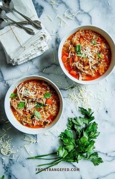 two bowls of soup with parmesan cheese on top and fresh parsley next to it