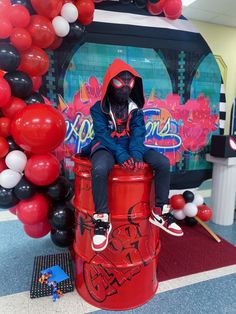 a person sitting on top of a red trash can in front of balloons and decorations