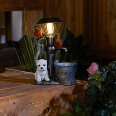 a small white dog sitting on top of a table next to a lamp and potted plant