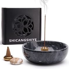 a black bowl with incense sticks in it next to an open box that says shinganshive