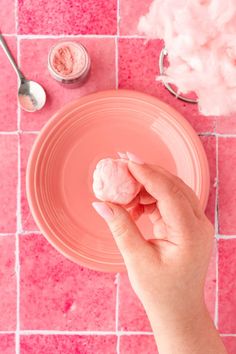 a pink plate with cotton on it and a hand holding a powdered doughnut