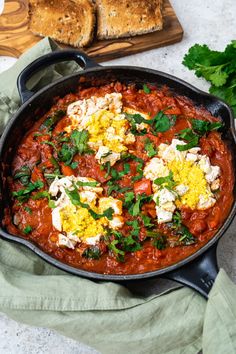 a skillet filled with meat and vegetables on top of a green cloth next to bread