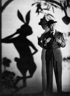 a man in a suit and hat standing next to a shadow of a rabbit on the wall