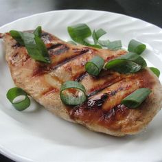 a white plate topped with meat covered in green leafy garnish and sauce