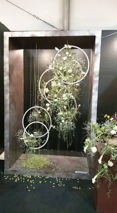 an arrangement of flowers and plants in a wooden box with metal rings hanging from the sides