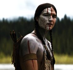 a native american man with white paint on his face and chest standing in front of water