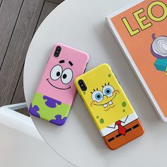 two cartoon phone cases sitting on top of a white table next to a book and chair