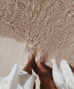 two people standing on the beach with their feet in the sand