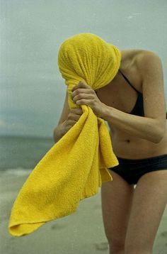 a woman in a bathing suit holding a yellow towel on the beach with her face covered