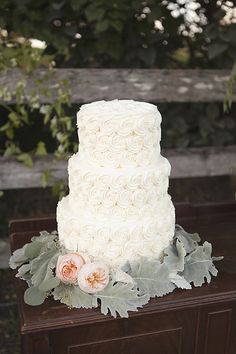 a three tiered white wedding cake sitting on top of a wooden table next to greenery