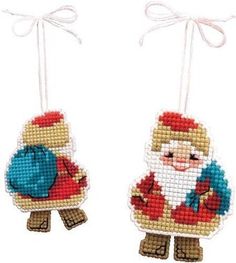 two cross stitch christmas ornaments hanging from strings, one with a santa clause on it