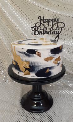 a white and black cake sitting on top of a metal stand with a happy birthday candle