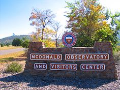 a sign for mcdonald observatory and visitors center in front of a road with trees on both sides