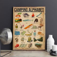 the camping alphabet poster is displayed on a table next to a lamp and some other items