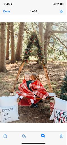 two children sitting in a teepee with christmas decorations on the ground and trees behind them