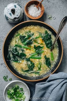 an overhead view of a bowl of soup with spinach and other ingredients on the side