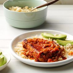 a white plate topped with meat covered in sauce and rice next to a bowl of vegetables