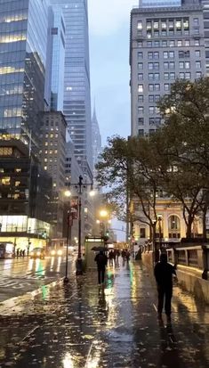 people are walking down the street on a rainy day with tall buildings in the background