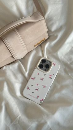 an iphone case sitting on top of a bed next to a handbag and purse