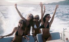 three women in bikinis on a boat waving to the camera with their arms up