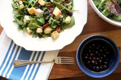 a salad with olives and croutons is on a plate next to a bowl of dressing