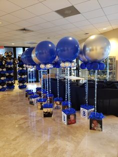 blue and silver balloons are hanging from the ceiling in front of black table cloths